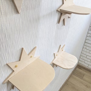 Op de afbeelding: Vier stervormige houten planken gemonteerd aan een witte muur. De planken zijn gemaakt van licht hout en hebben een afgeronde rand. Elke plank heeft een klein stervormig ontwerp in het midden.