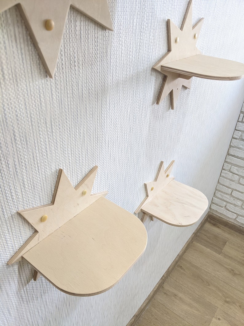 Op de afbeelding: Vier stervormige houten planken gemonteerd aan een witte muur. De planken zijn gemaakt van licht hout en hebben een afgeronde rand. Elke plank heeft een klein stervormig ontwerp in het midden.