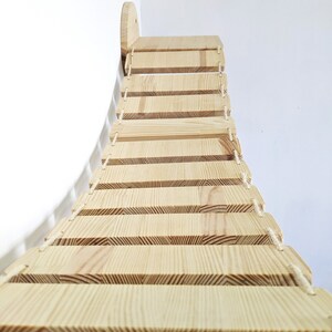 May include: A wooden cat climbing bridge with a curved design and rope accents. The bridge has multiple steps for cats to climb on.
