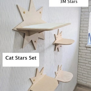 Op de afbeelding: Een set van vier houten kattenplanken in de vorm van sterren. De planken zijn gemonteerd aan een witte muur. De grootste plank is gelabeld "1XL Star + 3M Stars". De kleinere planken zijn gelabeld "Cat Stars Set".