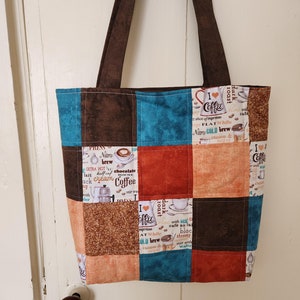 Peut inclure: Un sac fourre-tout en patchwork marron et bleu sur le thème du café. Le sac présente une variété d'images et de textes liés au café, notamment "J'aime le café", "Nitro Cold Brew" et "Torréfaction foncée".