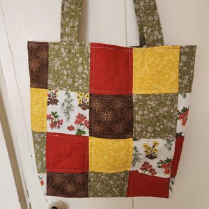 May include: A patchwork tote bag with a green, red, yellow, and brown color scheme. The bag has a floral pattern and is made of fabric.