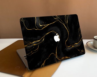 May include: A black laptop with a gold marble design on the lid. The laptop is closed and sitting on a brown leather case.