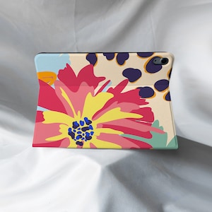 May include: A colorful floral design on a tablet case. The case features a large pink and yellow flower with a blue center, surrounded by smaller flowers and leaves. The background is a light beige with a subtle pattern.
