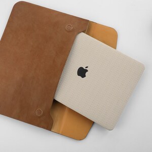 Puede incluir: Una funda de cuero marr&oacute;n con un interior de tela beige. La funda tiene una solapa que se cierra con un broche a presi&oacute;n. La funda est&aacute; dise&ntilde;ada para guardar una tableta o un port&aacute;til.