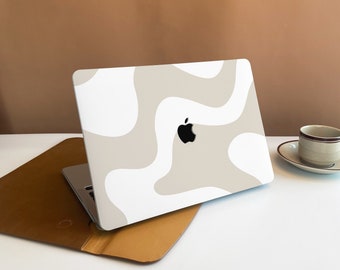 May include: A laptop computer with a white and beige abstract design on the lid. The laptop is closed and sitting on a brown leather case.