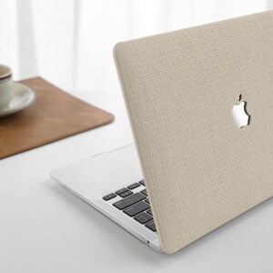 Puede incluir: Una funda para port&aacute;til beige con un acabado de tejido texturizado. La funda tiene un recorte para el logotipo de Apple.