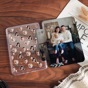 Könnte beinhalten: Eine transparente Handyhülle mit einem Muster aus mehreren Gesichtern und Sternen. Die Hülle ist geöffnet und zeigt ein Foto einer dreiköpfigen Familie, einem Mann, einer Frau und einem jungen Mädchen, die vor einem Holzschild stehen, auf dem "Meine wundervolle Familie" steht.