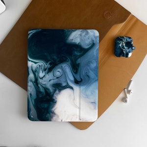 May include: A blue and white marbled iPad case with a brown leather folio case. The folio case has a small, black and white marbled case for AirPods.