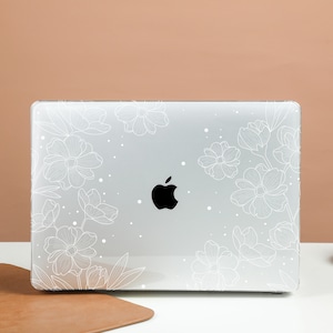 May include: A white laptop case with a floral design. The case features a white outline of flowers and leaves on a clear background. The Apple logo is visible on the laptop.