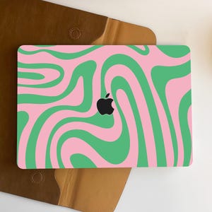Può includere: Una pelle per laptop rosa e verde con un motivo a spirale. La pelle ha un ritaglio per il logo Apple.