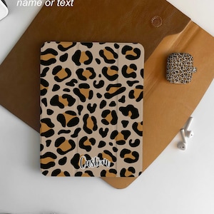 Puede incluir: Una funda para iPad de color beige con un diseño de estampado de leopardo con manchas negras y marrones. La palabra "Custom" está escrita en la funda. La imagen también muestra una funda para AirPod a juego y las palabras "Personalisation name or text".