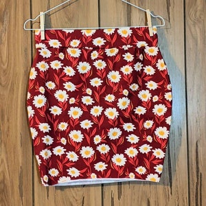 May include: A red skirt with a white daisy print. The skirt is hanging on a silver hanger.