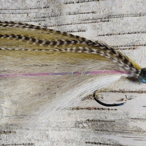 May include: A fly fishing lure with a brown and white feather body, a pink thread wrap, and a green bead head.