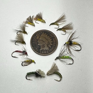 May include: A collection of 12 fly fishing lures, some with green, yellow, and red accents, arranged around a 1903 United States Indian Head penny.