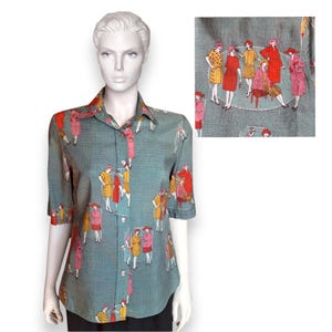 May include: A teal button-down shirt featuring a repeating pattern of figures in dresses and hats. The figures are in shades of red, yellow, and pink. The shirt has short sleeves and a collared neckline.