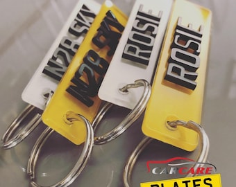 May include: Four rectangular keychains with metal split rings. Two keychains are white with black raised lettering reading N28 SKY and ROSIE. Two keychains are yellow with black raised lettering reading N28 SKY and ROSIE. A logo reads CAR CARE PLATES.