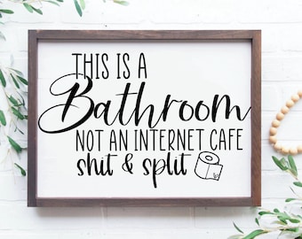 Puede incluir: Un letrero de baño enmarcado con el texto "THIS IS A Bathroom NOT AN INTERNET CAFE shit & split". El letrero tiene un fondo blanco con letras negras y un pequeño gráfico de rollo de papel higiénico. El marco es marrón.