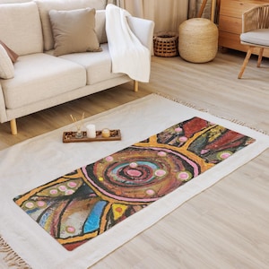 May include: A rectangular yoga mat featuring a vibrant, abstract design with concentric circles in shades of pink, blue, and brown. The surface is decorated with black outlines, geometric shapes, and small pink dots, creating a textured, hand-painted appearance across the entire mat.