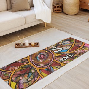 May include: A rectangular yoga mat featuring a vibrant, multi-colored abstract design with bold black outlines. The pattern includes circular and petal-like shapes in shades of red, yellow, blue, and purple, accented with small pink dots throughout.