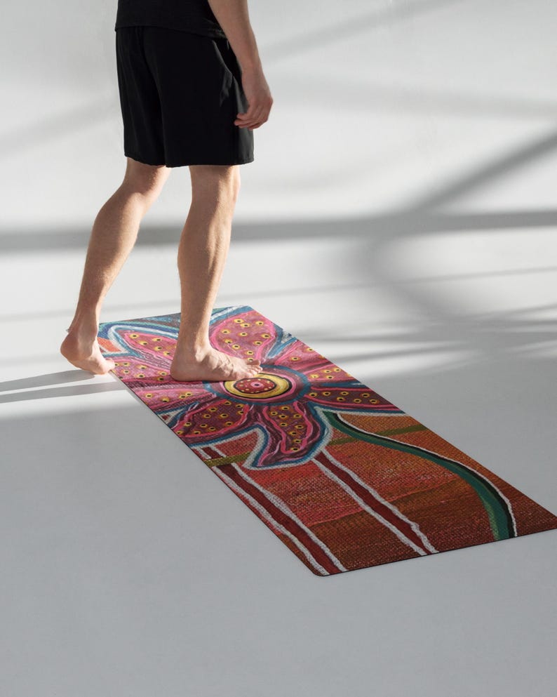 May include: A rectangular yoga mat featuring a vibrant, multi-colored floral pattern with a large pink and yellow central flower. The design includes textured orange, red, and green sections with white line accents, creating a detailed, artistic surface.