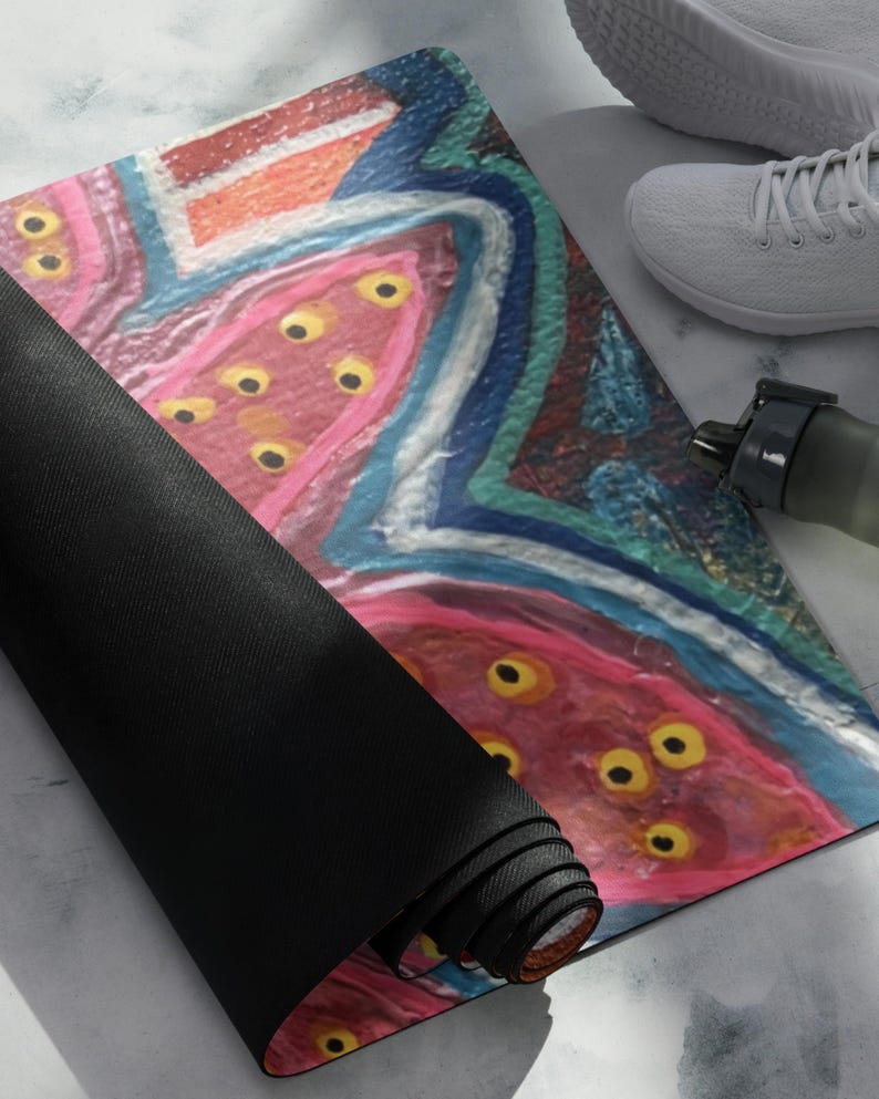 May include: A rectangular yoga mat featuring an abstract design with vibrant pink, blue, and orange brushstrokes. The surface is decorated with multiple yellow circular spots throughout the pink areas. The mat is partially rolled, revealing a solid black underside.