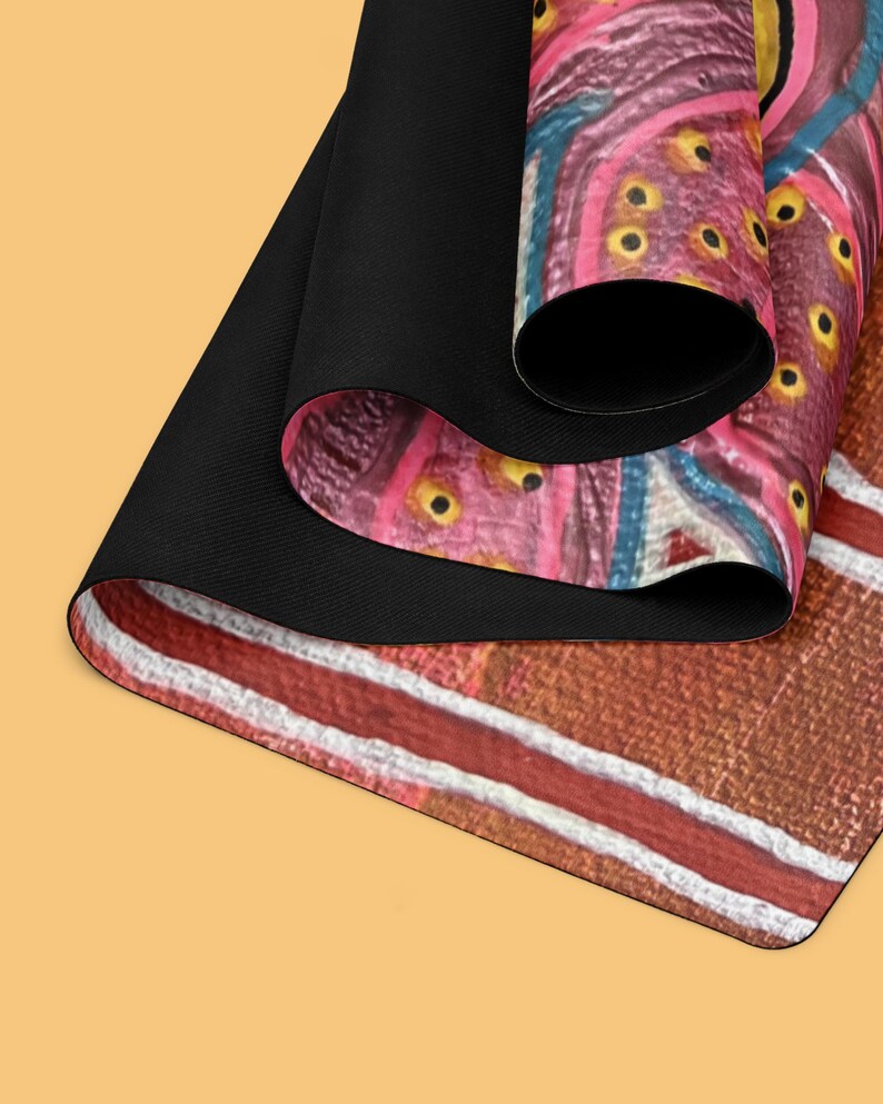 May include: A rectangular mat with a black underside and a rolled top edge. The surface features a vibrant abstract pattern with shades of pink, brown, and blue, accented by small yellow circular details and distinct white horizontal lines.