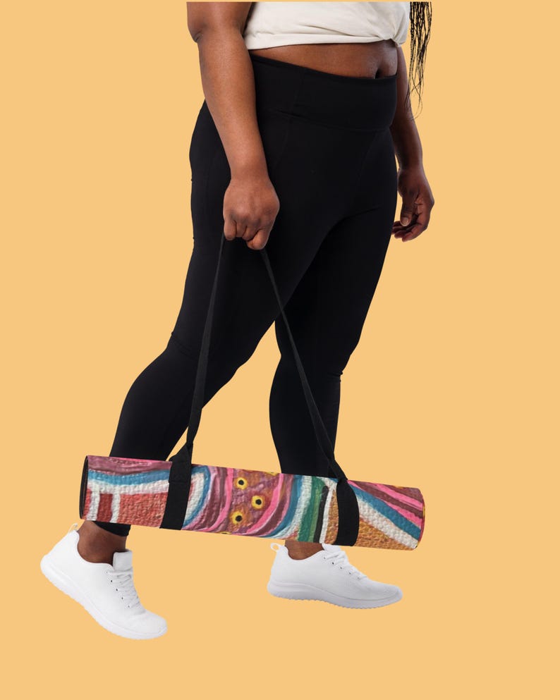 May include: A rolled yoga mat featuring a vibrant, abstract pattern with swirling lines and circular shapes in shades of pink, blue, brown, and white. The mat is equipped with a black carrying strap attached to the center for easy transport.