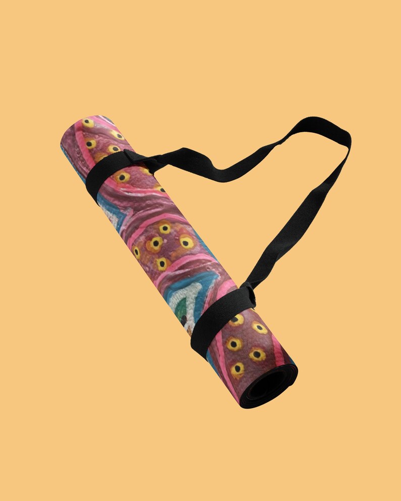 May include: A rolled yoga mat featuring a vibrant, abstract pattern with shades of pink, purple, and teal, accented by yellow circular motifs. The mat is secured with a black adjustable carrying strap that loops around the exterior for transport.
