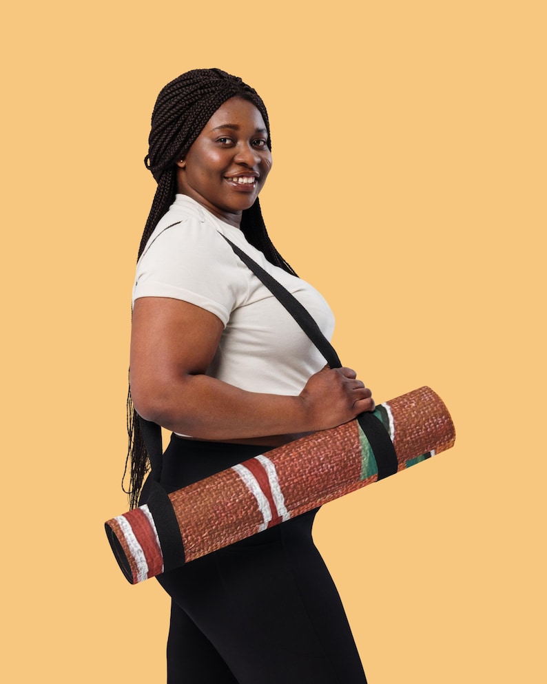 May include: A rolled yoga mat featuring a textured brown surface with white and red horizontal stripes and green accents. The mat is secured with a black carrying strap that loops over the shoulder, allowing for easy transport of the exercise equipment.