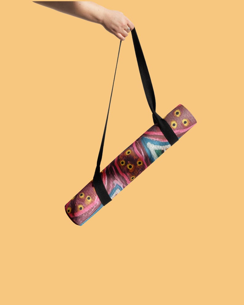 May include: A rolled yoga mat featuring a vibrant, abstract pattern with shades of deep red, pink, blue, and yellow circular motifs. The mat is suspended by a black adjustable carrying strap, showcasing a textured surface and a cylindrical shape.