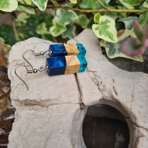 Puede incluir: Un par de pendientes de resina azul y madera con ganchos de plata. Los pendientes son de forma rectangular y tienen una parte superior de resina azul y una parte inferior de madera.