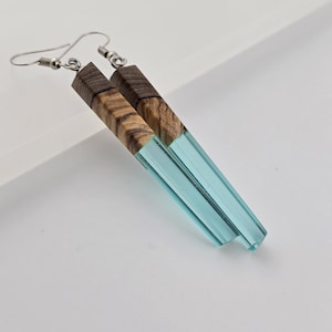 May include: A pair of dangle earrings with a light blue resin and wood design. The earrings are made of wood and resin and have a silver hook.