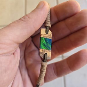 May include: A brown leather bracelet with a wooden charm featuring a green, blue, and black resin inlay.