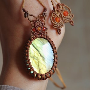 Könnte beinhalten: Eine braune Makramee-Kette mit einem großen ovalen Labradorit-Edelstein-Anhänger und kleineren Karneol-Perlen. Die Kette ist hinten mit einem Knoten gebunden.
