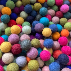 Könnte beinhalten: Eine große Sammlung bunter Filzkugeln in verschiedenen Schattierungen von Rot, Orange, Gelb, Grün, Blau, Lila und Rosa. Die Kugeln sind in einem zufälligen Muster angeordnet und schaffen so ein optisch ansprechendes und lebendiges Display.