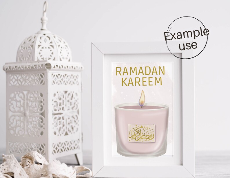 May include: A white frame with a gold inscription that reads "Ramadan Kareem". Inside the frame is a pink candle with a gold inscription in Arabic. The candle is lit and has a white flame.