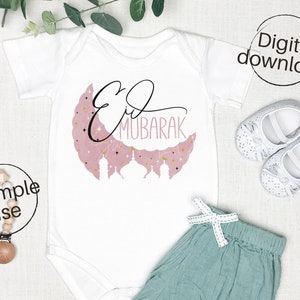 May include: White baby onesie with a pink crescent moon and gold stars. The text "Eid Mubarak" is written in black calligraphy on the moon.