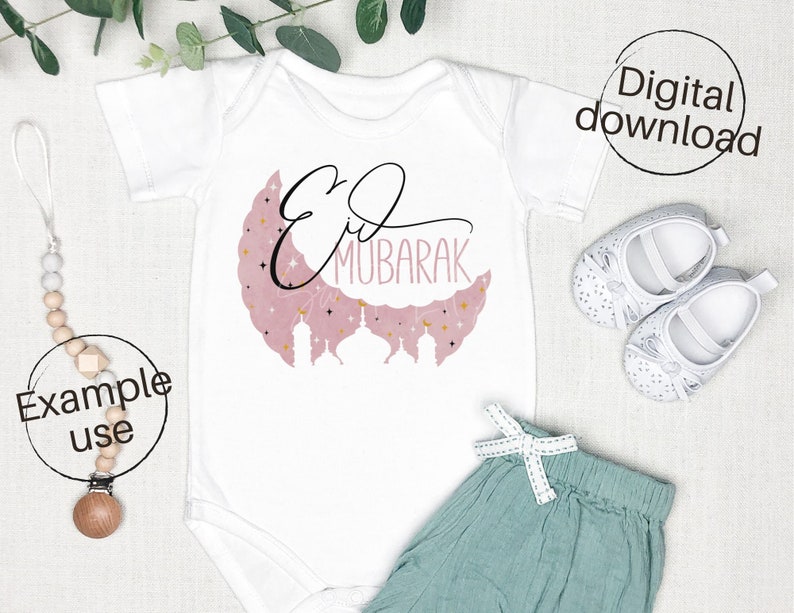 May include: White baby onesie with a pink crescent moon and gold stars. The text "Eid Mubarak" is written in black calligraphy on the moon.