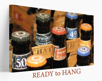 May include: A close-up of a wooden crate filled with various beer bottles. The bottles have different colored caps and labels, including a bottle labeled "Hanse" with a caramel flavor. The crate is on a wooden surface.