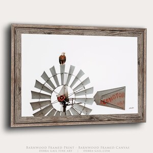 May include: A framed print featuring a bald eagle perched atop a metal windmill. The windmill has a circular fan with many blades and a tail fin with the red text AERMOTOR USA. The frame is made of weathered brown barnwood with a rustic texture.