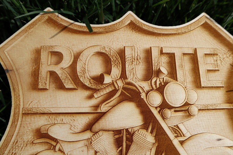 May include: A wooden sign with the word "ROUTE" carved into it. The sign is shaped like a shield and features a motorcycle with a headlight and handlebars.