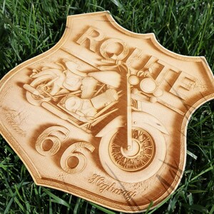 May include: A wooden sign with a Route 66 theme. The sign is shaped like a shield and features a motorcycle with a rider. The text "Route 66 Highway" is engraved on the sign.