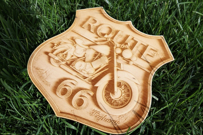 May include: A wooden sign with a Route 66 theme. The sign is shaped like a shield and features a motorcycle with a rider. The text "Route 66 Highway" is engraved on the sign.