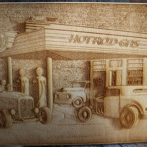 May include: A wood carving of a vintage gas station with the sign "HOT ROD GAS" above the entrance. There are three cars parked in front of the station, including a hot rod with a driver in the seat.