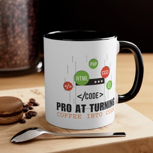 May include: White coffee mug with a black rim and handle. The mug features a graphic of code with the text "PRO AT TURNING COFFEE INTO CODE".