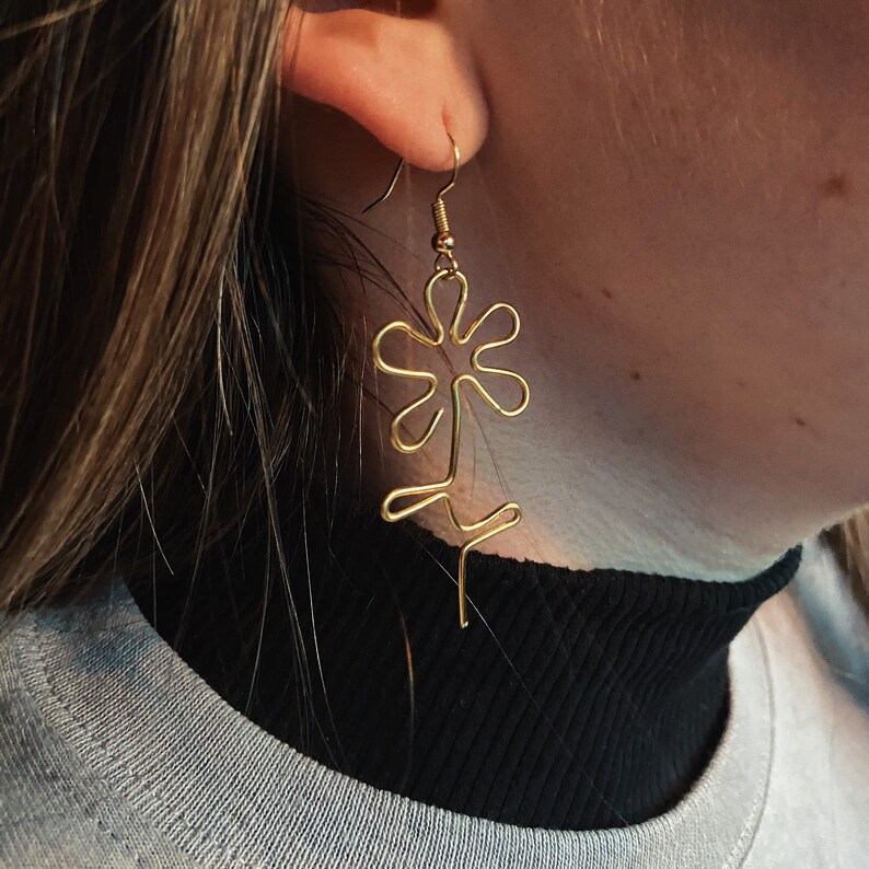 Może przedstawiać: Złote kolczyki w kształcie kwiatu z delikatnym wzorem z drutu.