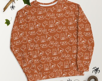 May include: A long-sleeved, orange sweatshirt with a white print of cats dressed as ghosts. The print is repeated all over the sweatshirt.