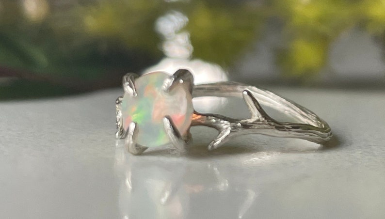 May include: A silver ring with a white opal gemstone set in a branch-like design.