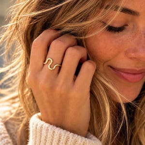 May include: A gold ring with a smooth, continuous wavy or serpentine design. The band features a polished metallic finish and a consistent rounded profile that curves back and forth in a repeating pattern around the finger.